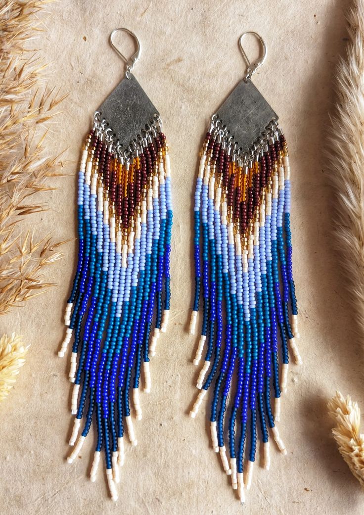 two pairs of beaded earrings sitting on top of a table next to dried grass