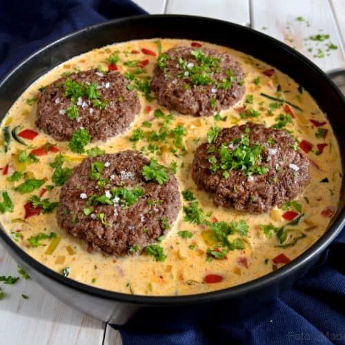 some meat patties are in a skillet with cheese and parsley on top