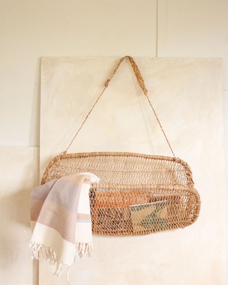 a woven basket hanging on the wall with a towel in front of it and a blanket folded up next to it