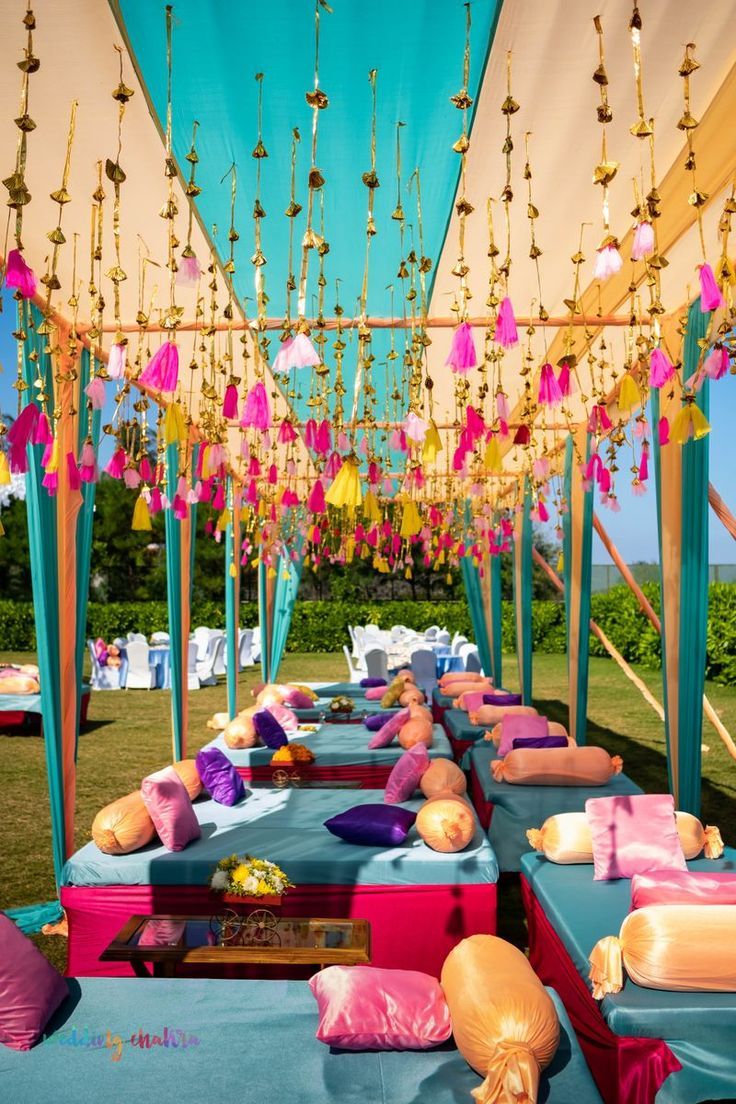 an outdoor event with lots of tables and chairs covered in blue linens, colorful decorations and hanging lights