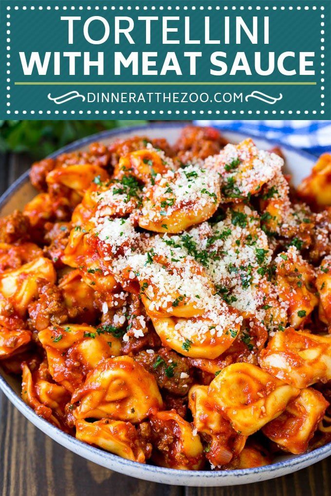 tortelli with meat sauce in a bowl on a table next to parmesan cheese