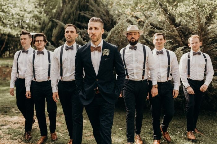 a group of men standing next to each other wearing suits and bow ties in front of trees