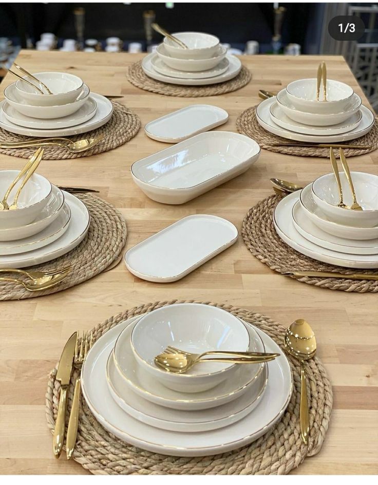 a wooden table topped with white plates and goldware