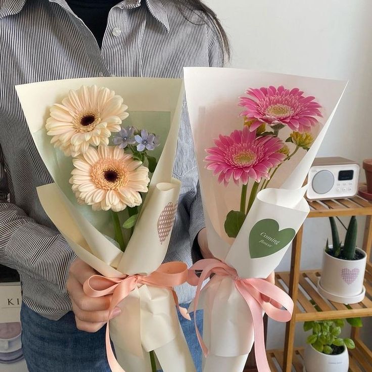 a person holding two bouquets of flowers in their hands, one with pink and white daisies on it