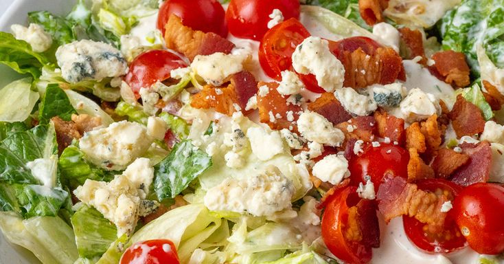 a salad with tomatoes, lettuce and bacon on it in a white bowl