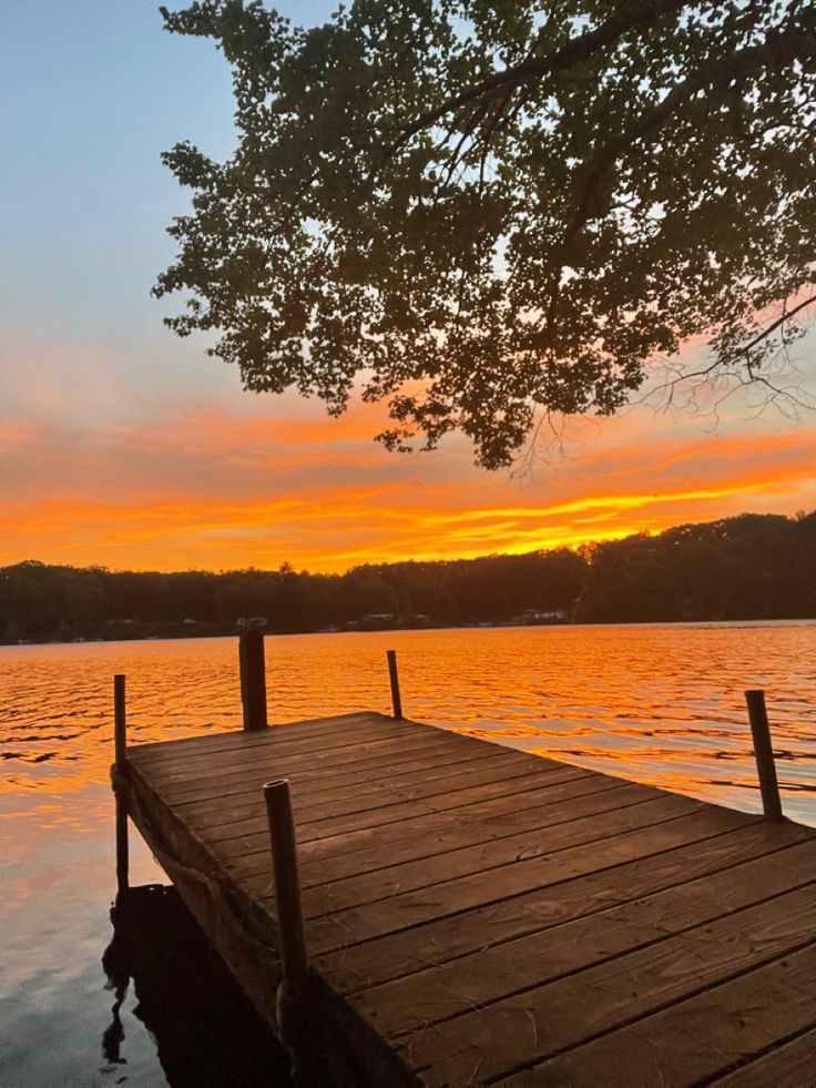 a wooden dock sitting on top of a lake under a sunset over the water with trees