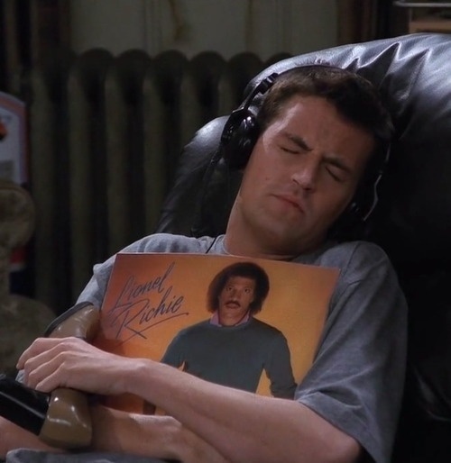 a man laying in a chair with his head propped up on a book and wearing headphones