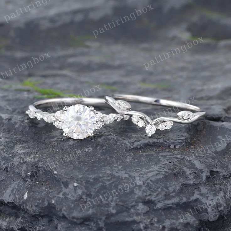 two wedding rings with leaves on them sitting on top of a stone slab in the grass