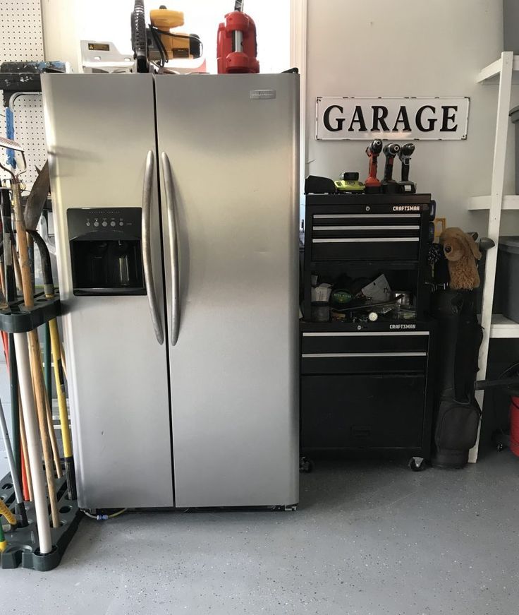 a large metallic refrigerator freezer sitting inside of a garage next to a toolbox