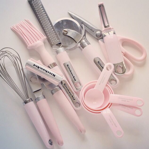 pink kitchen utensils and whisks are arranged on a white table top