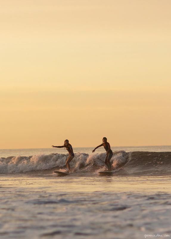 two people riding surfboards on top of a wave in the ocean at sunset or dawn