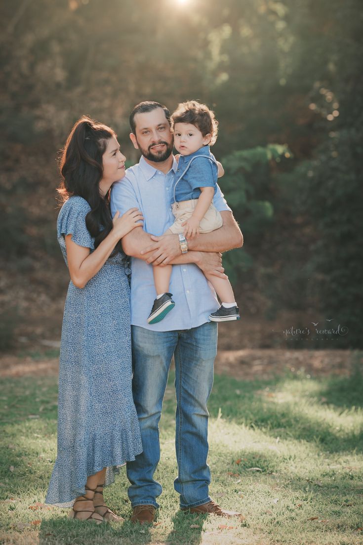 a man and woman holding a baby in their arms while the sun shines behind them