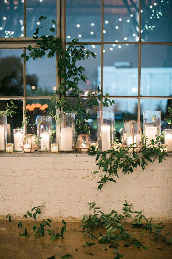 candles and greenery are arranged on the window sill in front of a brick wall