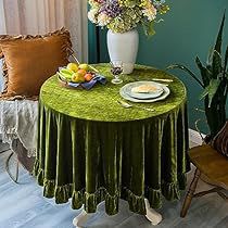 a green table cloth on top of a round table in front of a vase with flowers