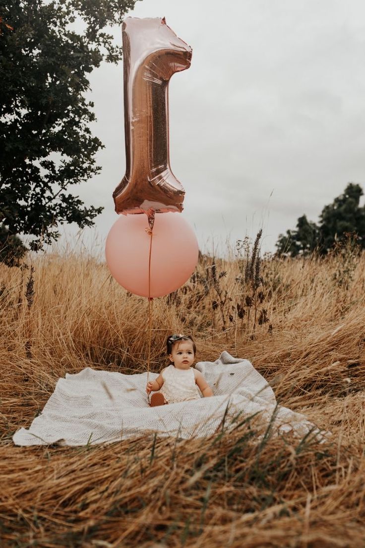 a baby sitting on a blanket in the middle of a field with an 11 balloon