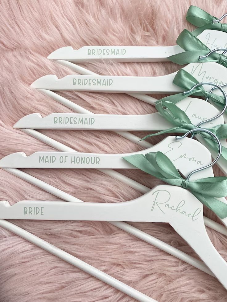 four bridesmaid hangers with green bows and names on them sitting on a pink furnishing