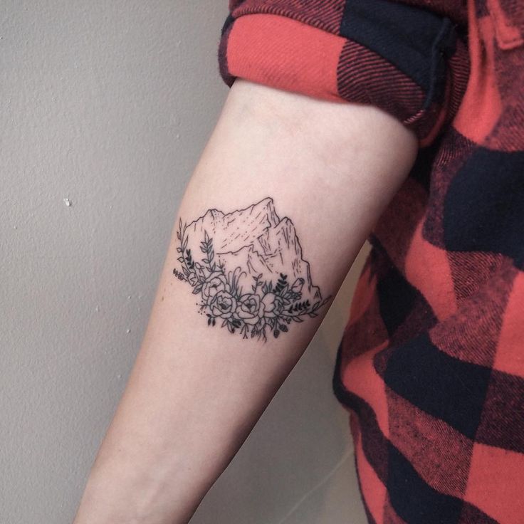 a woman's arm with a tattoo on it that has mountains in the background