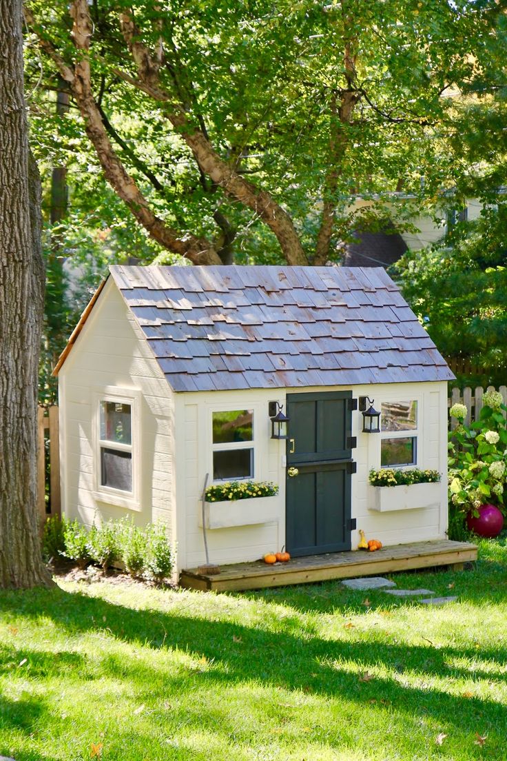 a small white house sitting in the middle of a lush green yard next to a tree