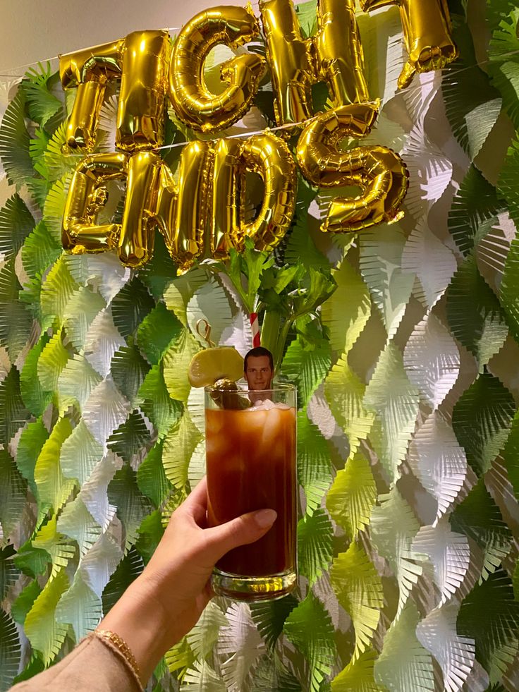 a person holding a drink in front of a wall with foil balloons