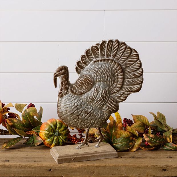 a metal turkey figurine sitting on top of a wooden table next to autumn leaves