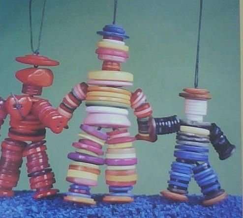 three toy figures made out of different colored yarn spools hanging from strings on a blue surface