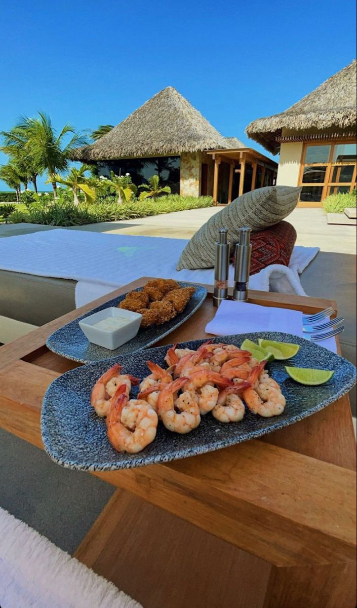 a plate with shrimp and other food on it next to a table in front of a pool