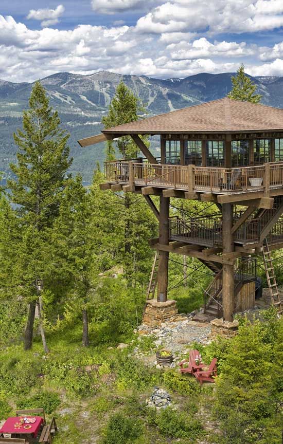 a large wooden structure sitting on top of a lush green hillside next to trees and mountains