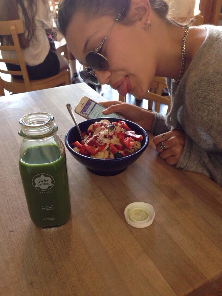 a woman sitting at a table with a bowl of food and a bottle of juice