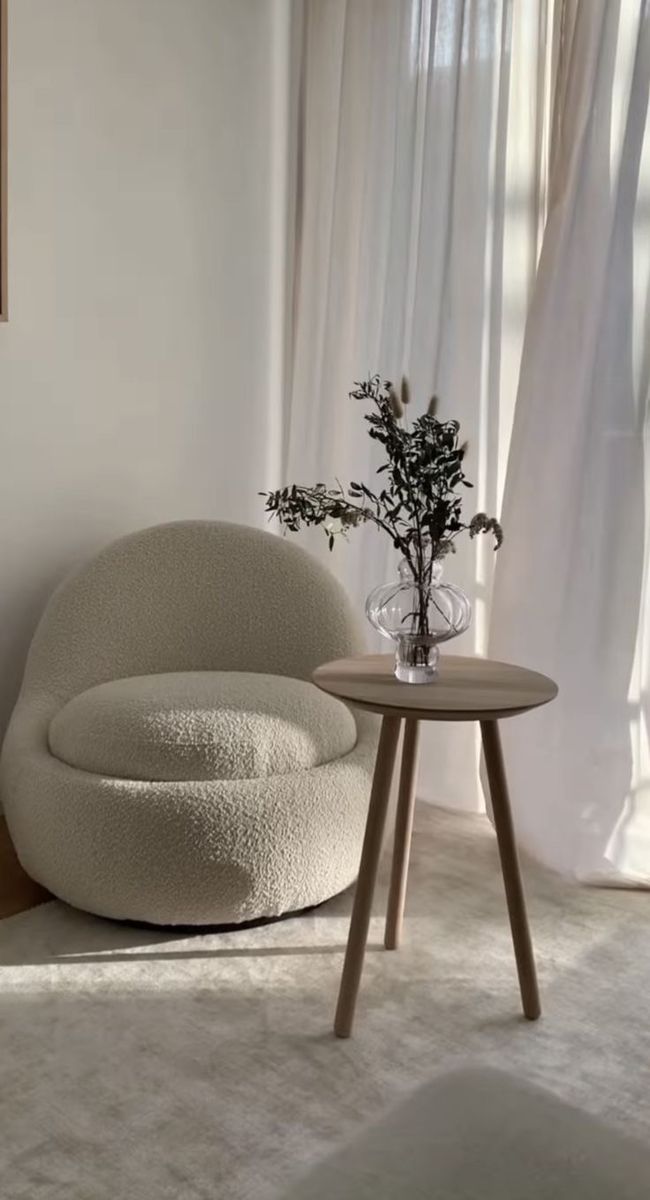 a white chair and table in a room with curtains on the window sill behind it