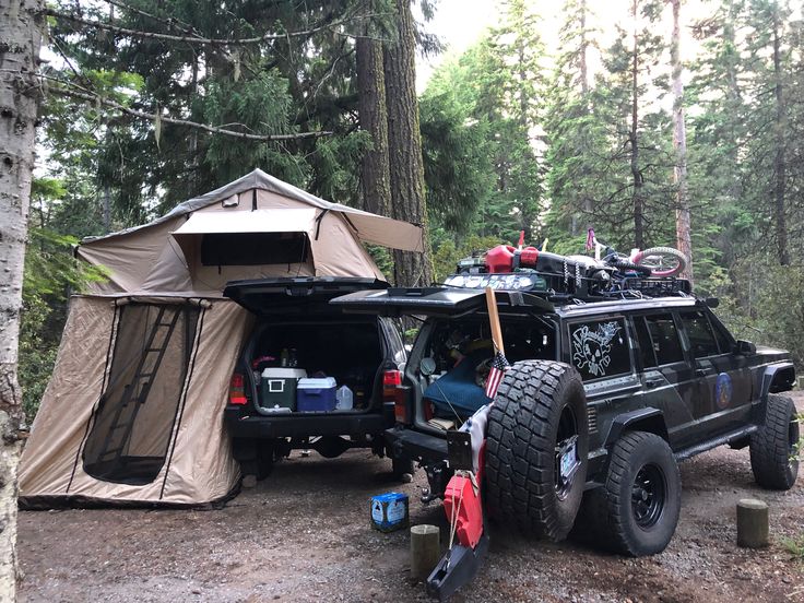 an suv parked next to a tent in the woods