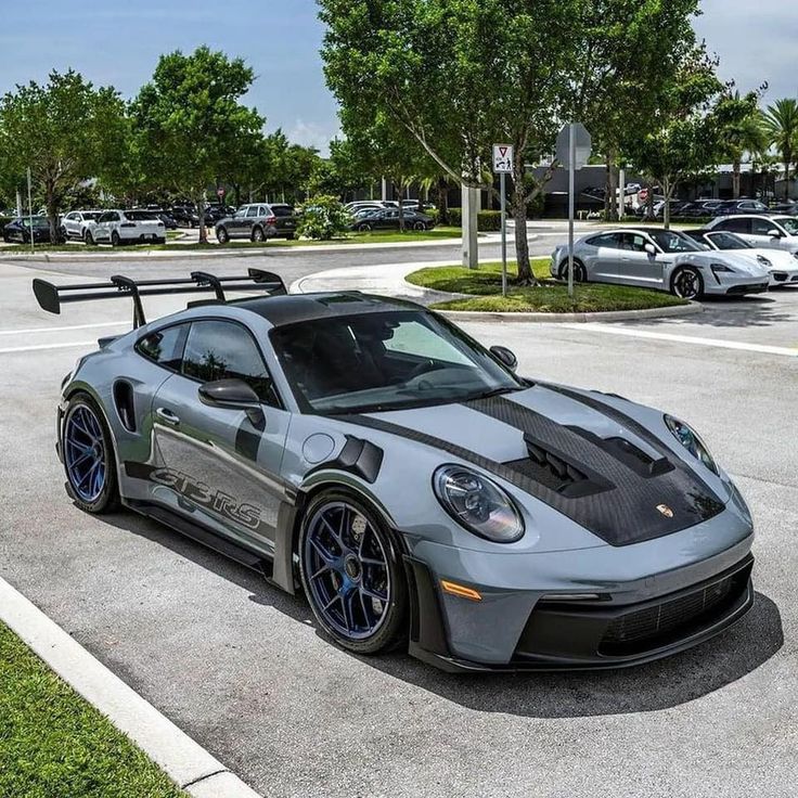 a gray sports car parked in a parking lot next to trees and cars on the street