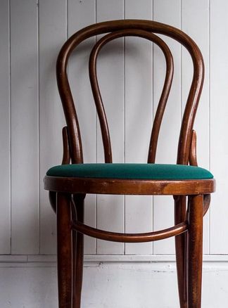 a wooden chair with a green seat pad on the back of it, against a white wall