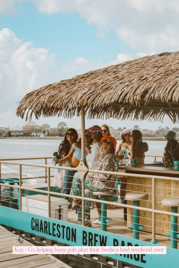 a group of people standing on top of a wooden pier next to the ocean under a thatched umbrella