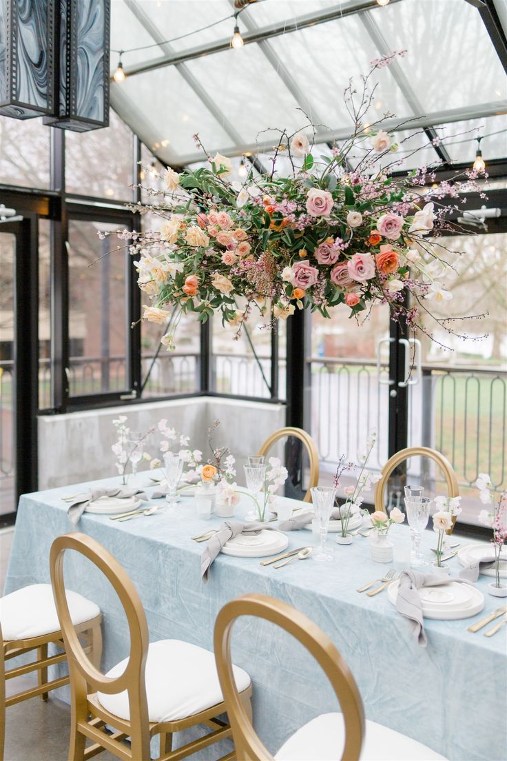 a dining room table set up with flowers and place settings in front of large windows