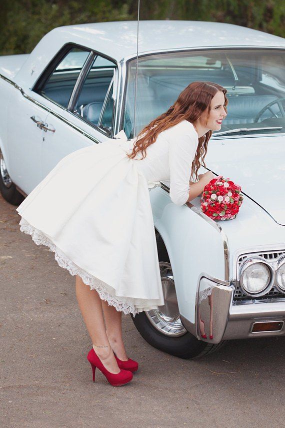 a woman in a white dress leaning on the hood of a vintage car with flowers