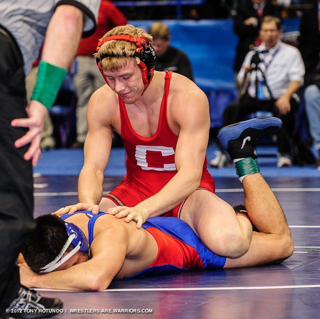 a wrestling match with two wrestlers in red and blue uniforms, one wrestler is on the ground