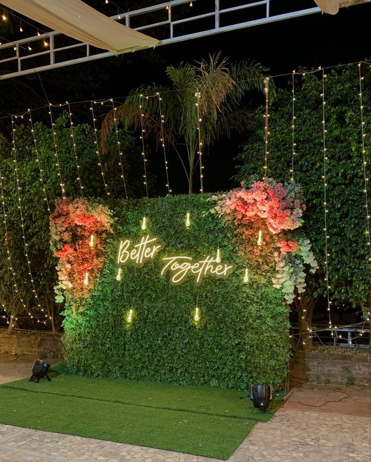 an artificial garden wall with flowers and lights on it's sides is lit up at night