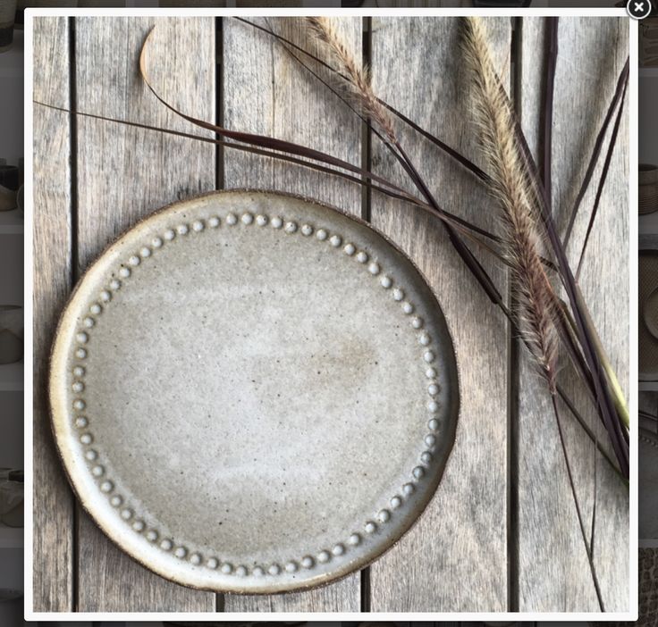 a white plate sitting on top of a wooden table next to dried grass and leaves