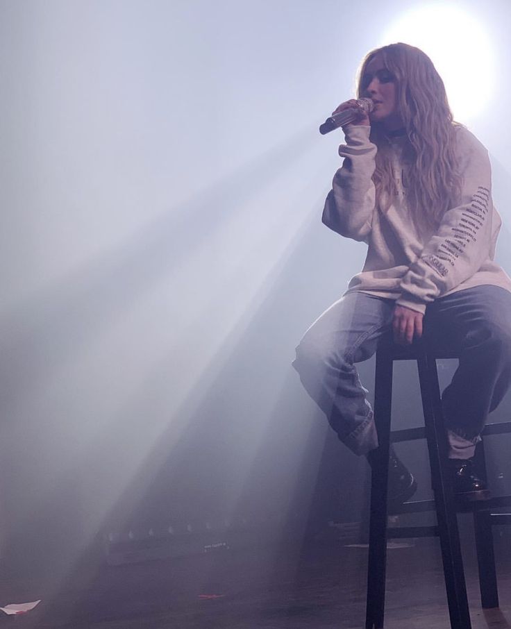 a woman sitting on top of a stool while holding a microphone in her hand and singing