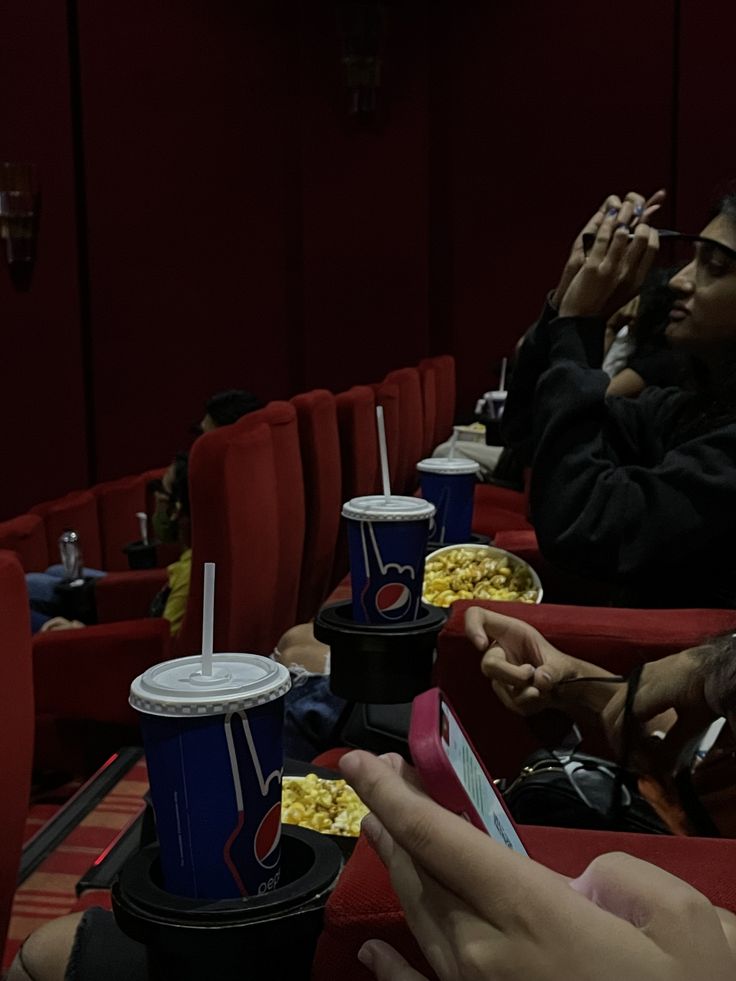 people are sitting in the movie theater and eating popcorn, watching movies on their cell phones