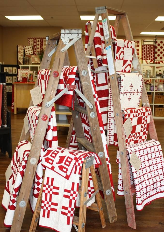 several red and white quilts are stacked on wooden ladders in a store display