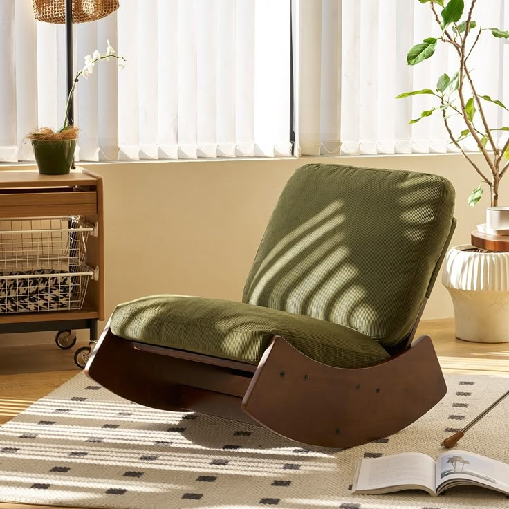 a rocking chair with a book on the floor in front of a window and a plant