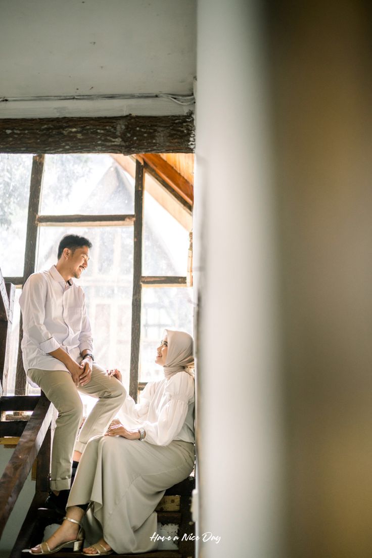 a man and woman sitting on top of some stairs in front of a window with sunlight coming through the windows