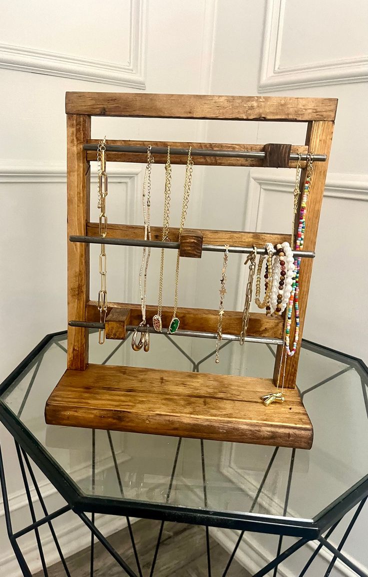 a glass table topped with a wooden bench and necklaces hanging from it's sides