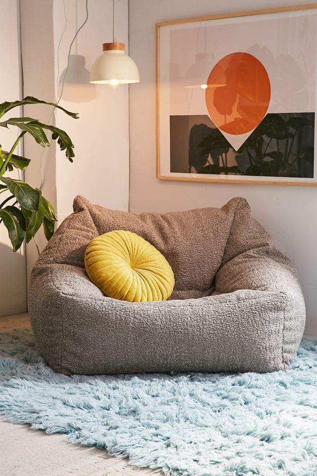 a dog bed with a yellow pillow on top of it in a living room next to a potted plant