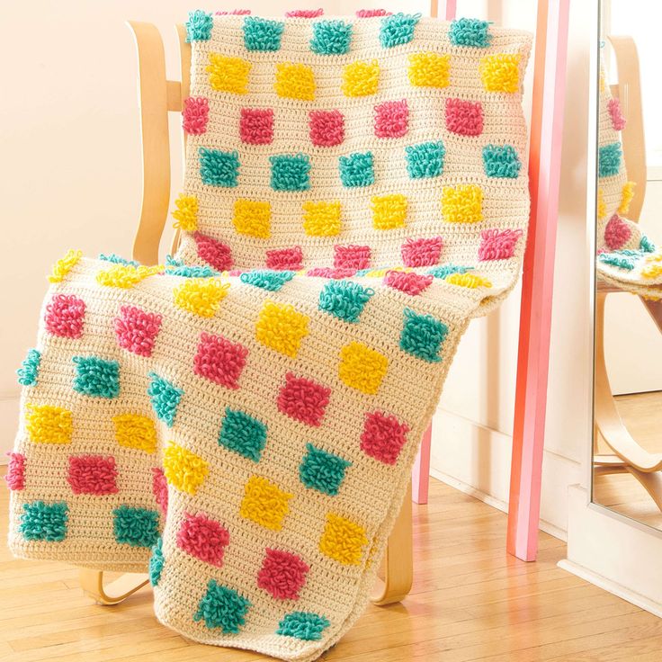 a crocheted blanket sitting on top of a wooden chair next to a mirror