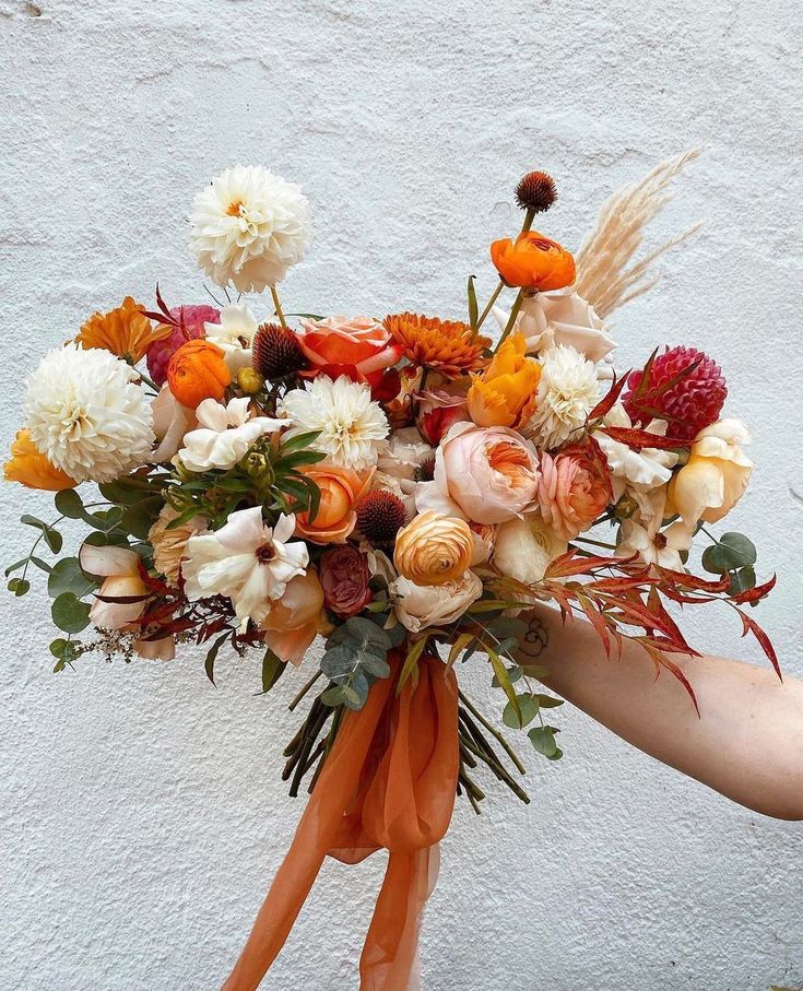 a woman holding a bouquet of flowers in her hand with an orange ribbon around it