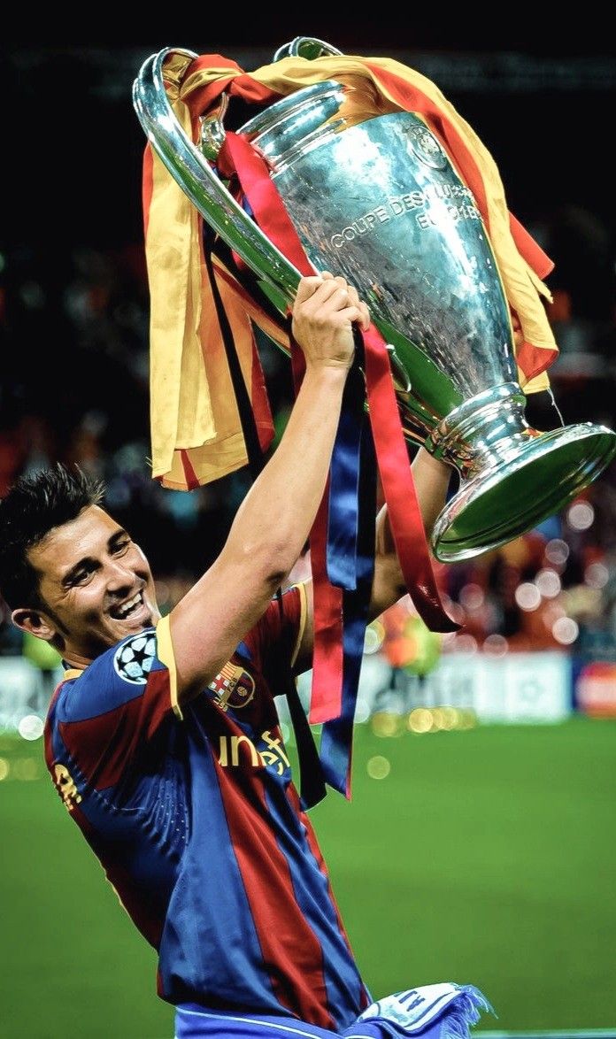 a man holding up a trophy on top of a soccer field with his hands in the air