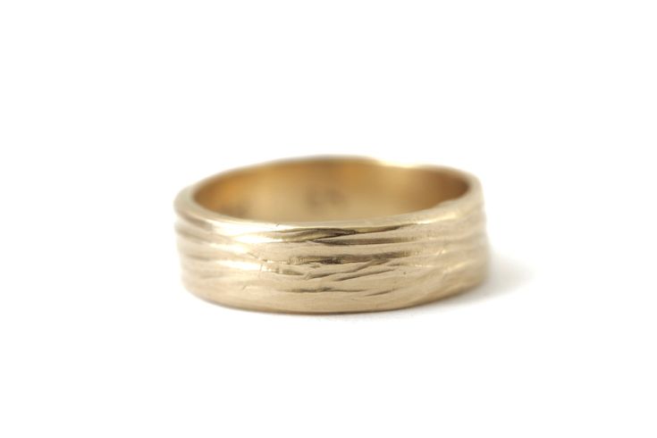 a gold wedding ring with wavy lines on the outside and inside, set against a white background