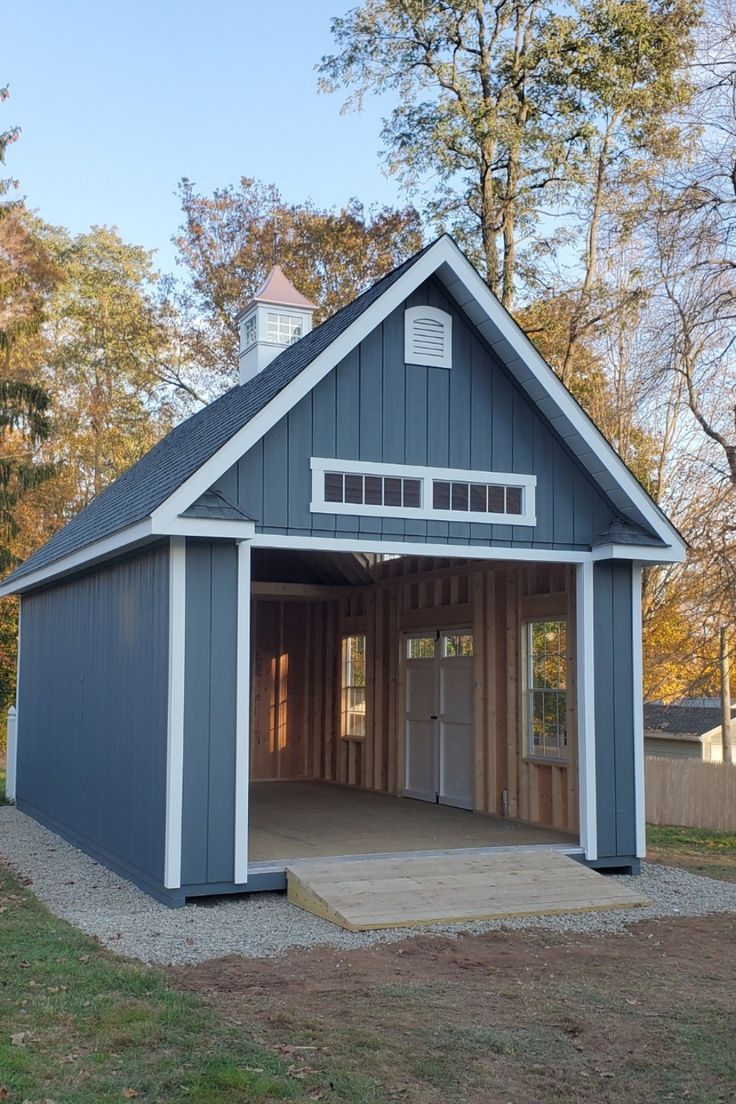 a blue and white garage with an open front door on the side, surrounded by trees